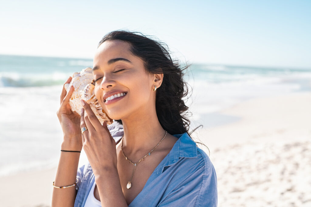 Young woman listening the sound of the ocean with a seashell