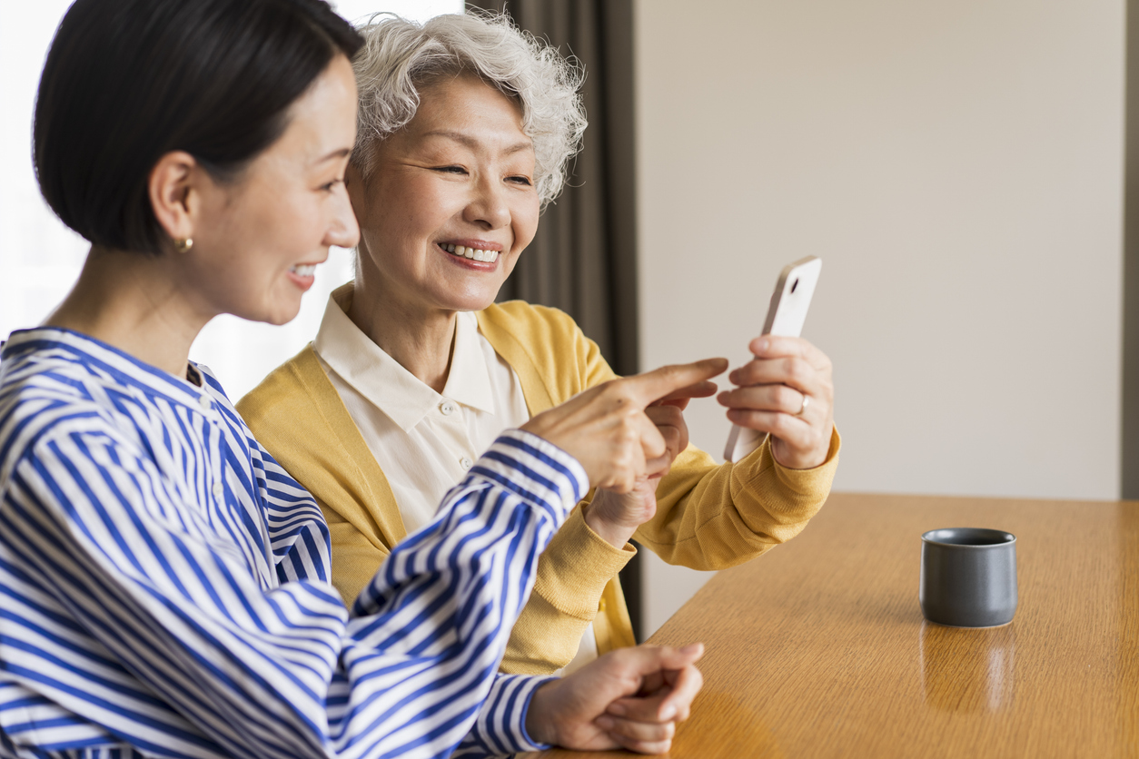 A young woman teaches a senior woman how to use a mobile phone in the living room.