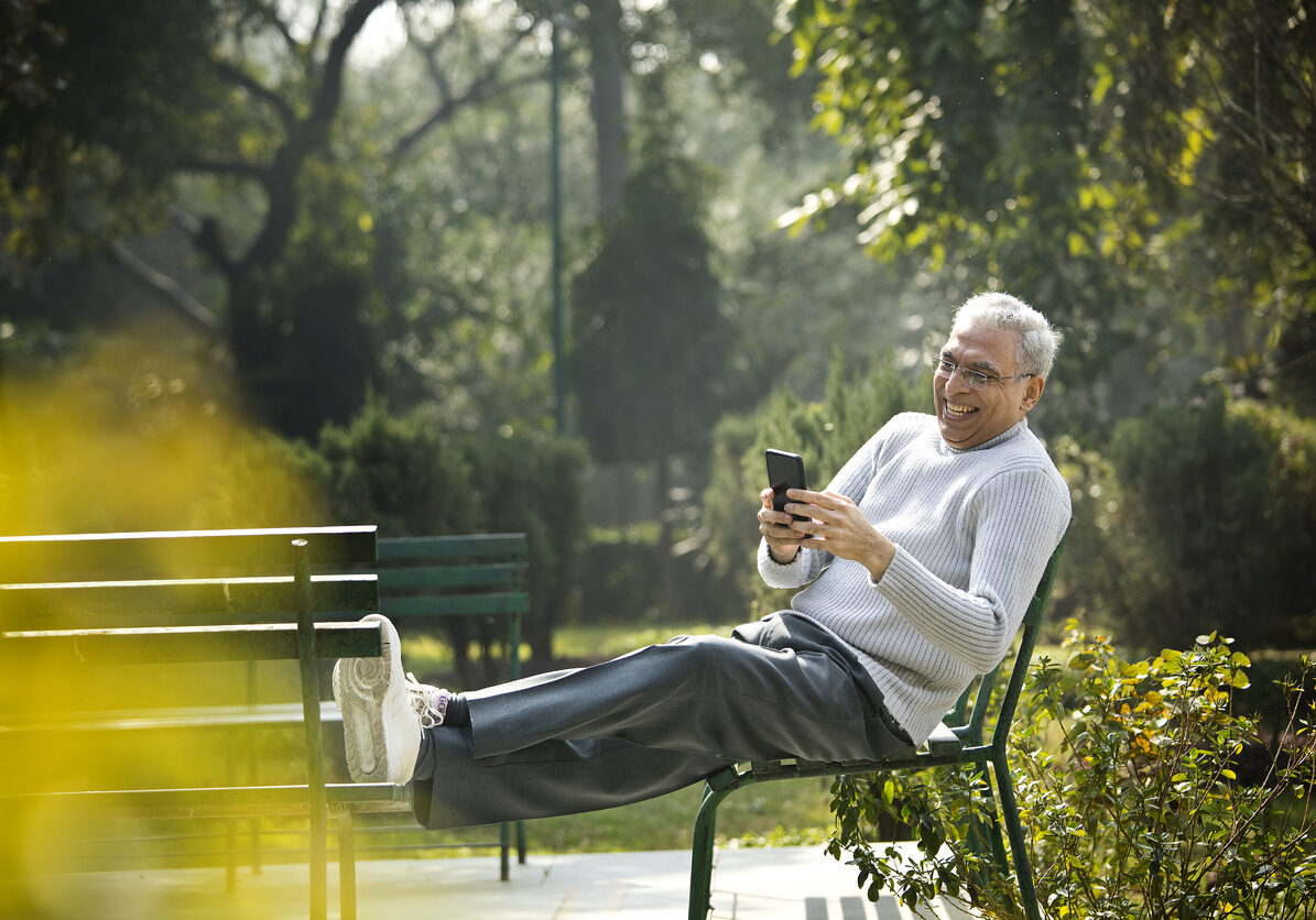 Senior man having fun using mobile phone at park Senior man laughing while using mobile phone and relaxing at park